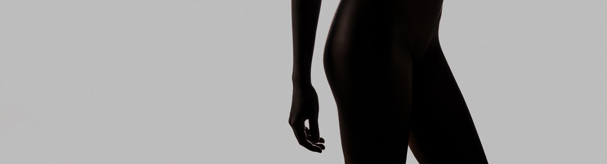 Editorial backlit silhouette of a female lower body on a neutral studio backdrop, representing intimate rejuvenation care by Dr. Jason Emer